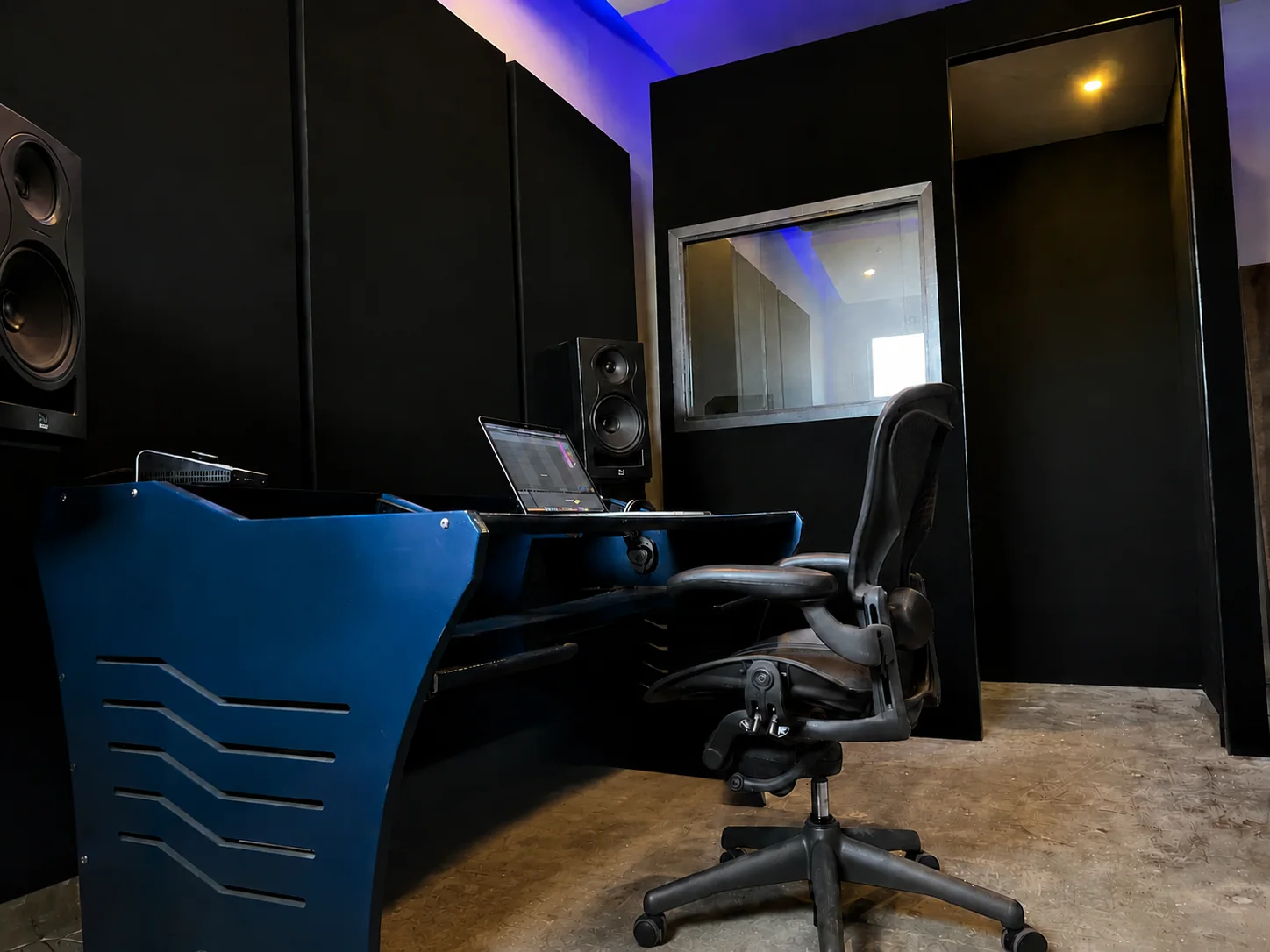 Studio B workstation beside the dedicated vocal-booth window and doorway